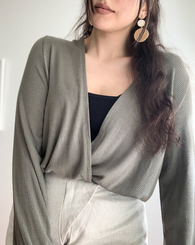 Ribbed reversible wrap top in the colour olive worn with beige pants.