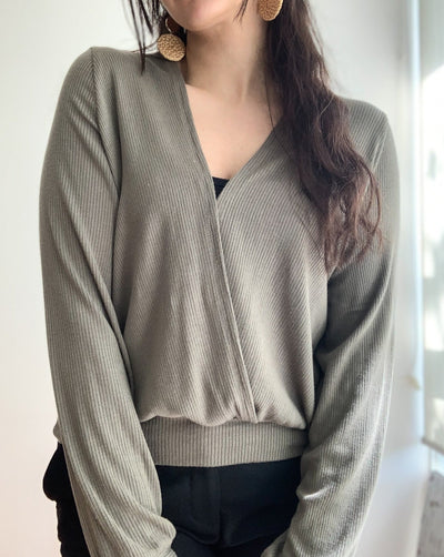 Ribbed reversible wrap top in the colour olive worn with beige pants.