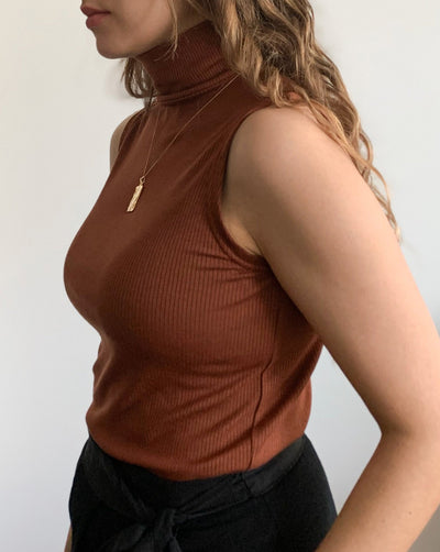 Sustainable Tencel modal ribbed sleeveless pecan-coloured turtleneck worn with black trousers.