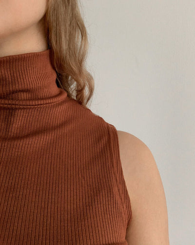 Sustainable Tencel modal ribbed sleeveless pecan-coloured turtleneck worn with black trousers.